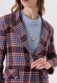 Blazer met pied-de-poule patroon in bordeauxrood, blauw en crème. Voorzien van revers met inkeping, twee voorzakken en een metalen knoopsluiting.