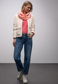 Veste en polaire crème avec deux poches avant, pull rose, jean droit bleu, et baskets blanches ; écharpe superposée rose et corail.
