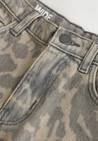 Prim-plan cu blugi din denim gri deschis, cu croială largă, care prezintă nasturele, bucle pentru curea, marginea superioară și o parte din buzunarul frontal cu detalii vizibile ale cusăturilor.