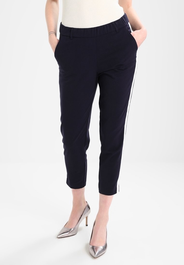 Granatowe spodnie w luźnym kroju, z elastycznym pasem, kieszeniami po bokach oraz kontrastującymi białymi paskami wzdłuż boków. Połączone z srebrnymi szpilkami.