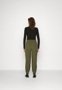 Svart långärmad topp och gröna avslappnade byxor med elastisk midja och manchetter vid anklarna, bärs tillsammans med svarta sneakers.