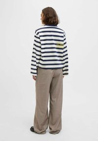 A woman stands with her back to the viewer, wearing a striped top and wide-legged pants. The top features a yellow printed message.