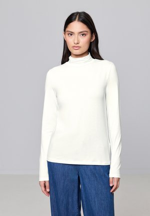 Witte turtleneck met lange mouwen, gemaakt van een gladde stof en met een slim-fit ontwerp, gecombineerd met wijde denim broeken. Neutrale achtergrond.