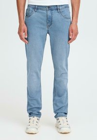 Gai zila džinsu bikses ar taisnu kājām, ar priekšējām un aizmugurējām kabatām, un smalku izšuvumu detaļām. Valkātas kopā ar baltām sporta kedām.