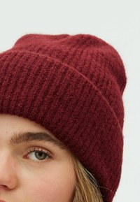 Căciulă tricotată burgundy din lână moale, cu o textură ribată și vârf conic. Are o croială strânsă în jurul capului.