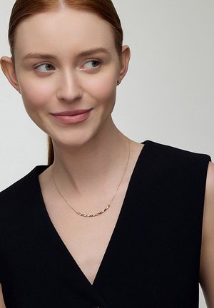 Złoty naszyjnik o skręconym wzorze, noszony przez osobę w czarnej bluzce. Łańcuszek jest delikatny z gładkim wykończeniem.