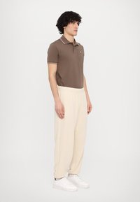 Brown polo shirt with white collar trim, paired with loose-fitting cream sweatpants and white sneakers. Smooth textures and casual design.