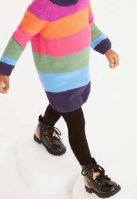 Mehrfarbiger gestreifter Pullover aus Wollmischung mit langen Ärmeln. Schwarze Lackstiefel mit Regenbogen-Details und kontrastierenden Schnürsenkeln.