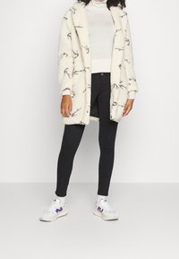 Abrigo de felpa blanca con diseño de ramas negras, combinado con un ligero cuello de tortuga, leggings negros y zapatillas blancas con acentos morados.