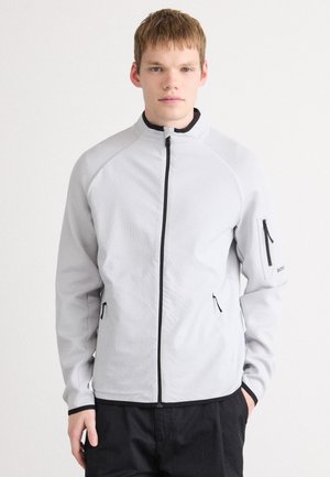Lichtgrijze fleece jas met een hoge kraag, zwarte rits en ritszakken aan de zijkanten. Bevat zwarte accenten en een logo op de mouw.