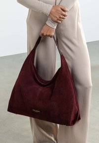Burgundy suede hobo bag with a spacious, slouchy design and dark leather accents; features subtle branding on the front.