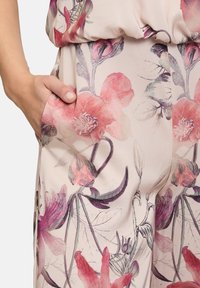 Bloemen jumpsuit van zachte stof met roze en paarse bloesems op een lichte achtergrond, voorzien van een zijzak en een losse, vloeiende pasvorm.