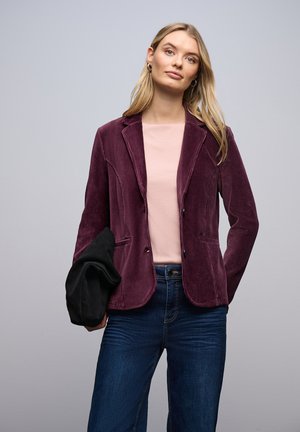 Blazer in velluto a coste bordeaux con rever a scollatura, due tasche frontali e design aderente; indossato sopra una camicia rosa chiaro e abbinato a jeans scuri.