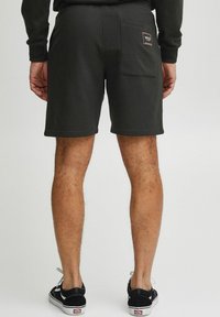 Mørkegrå bomuldsshorts med en baglomme og et logo-patch, der har en afslappet pasform og en glat tekstur. Båret med sorte sneakers.