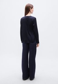 Μπλούζα από μετάξι σε ναυτικό μπλε χρώμα με μακριά μανίκια, στρογγυλή λαιμόκοψη και λεία υφή, συνδυασμένη με παντελόνι τζιν σκούρου μπλε με φαρδιά μπατζάκια και ορατή ραφή.