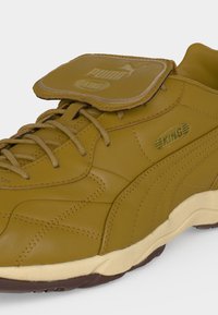 Κίτρινο δερμάτινο αθλητικό παπούτσι Puma King με ταιριαστά κορδόνια, πατιλέτα πάνω από το κολάρο της φτέρνας και μπεζ σόλα με σκούρο καφέ πέλμα.