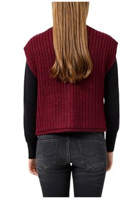 Vīnkrāsas adīta veste ar teksturētu rakstu, īsām piedurknēm, valkāta virs melnas garām piedurknēm krekla, kombinēta ar tumši pelēkiem džinsiem.