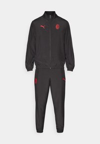 Črn trenirka z rdečimi poudarki. Zip-up jakna z visokim ovratnikom; hlače imajo elastične manšete. Logotip na jakni in hlačah. Gladka tekstura tkanine.