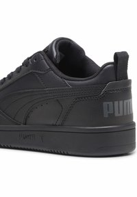 Baskets noires en cuir avec une finition texturée, des lacets plats et un col rembourré. Le logo "PUMA" est embossé en gris sur le talon.