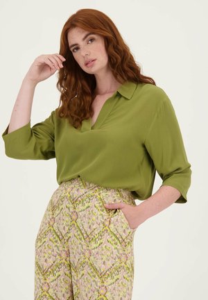 Blouse verte à col, avec un décolleté en V et des manches trois-quarts, associée à un pantalon large à motifs roses et verts présentant des designs géométriques.