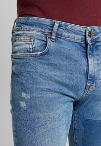 Blå jeans i denim med en tvättad och lätt urblekt look, med en klassisk design med fem fickor, synliga sömmar och subtila slitningsdetaljer.