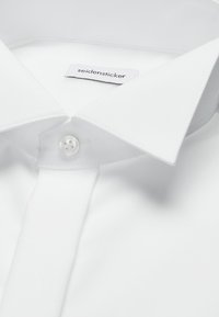 Weißes Hemd mit spitzem Kragen, oberster Knopf geschlossen und Markenetikett mit der Aufschrift "seidensticker" im Kragen.