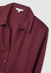 Blusa a maniche lunghe bordeaux realizzata in tessuto morbido, con colletto a punta e chiusura con bottoni, dal taglio rilassato. Etichetta della taglia visibile: 2XL.