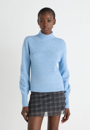 Lys blå, ribbet turtleneck sweater med lange ærmer; kombineret med en sort ternet miniskørt med bølget kant.