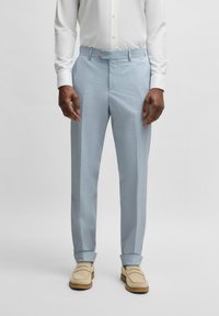 Ljusblå mönstrade byxor i mjukt tyg, med en skräddarsydd passform och knappstängning i midjan. Bäraren har på sig beige skor.