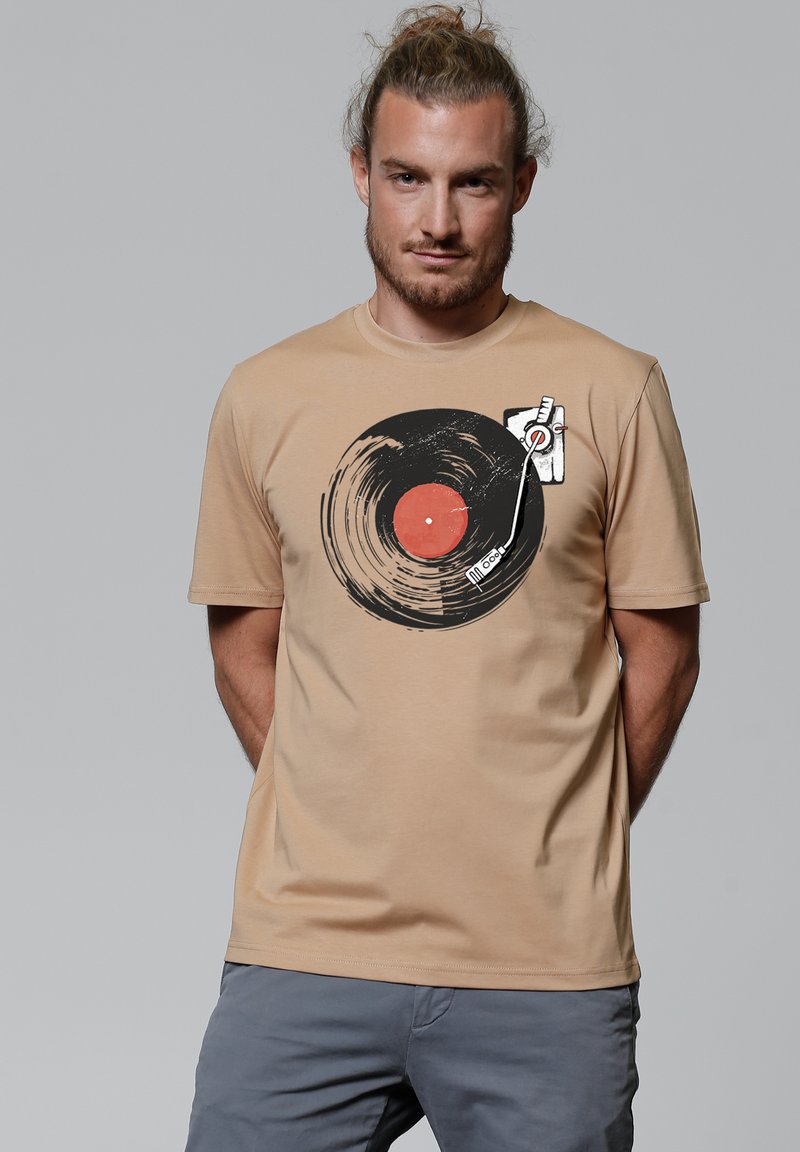 Beige katoenen t-shirt met een grote afbeelding van een zwarte vinylplaat met een rode center en een stylus. Korte mouwen, ronde halsontwerp.