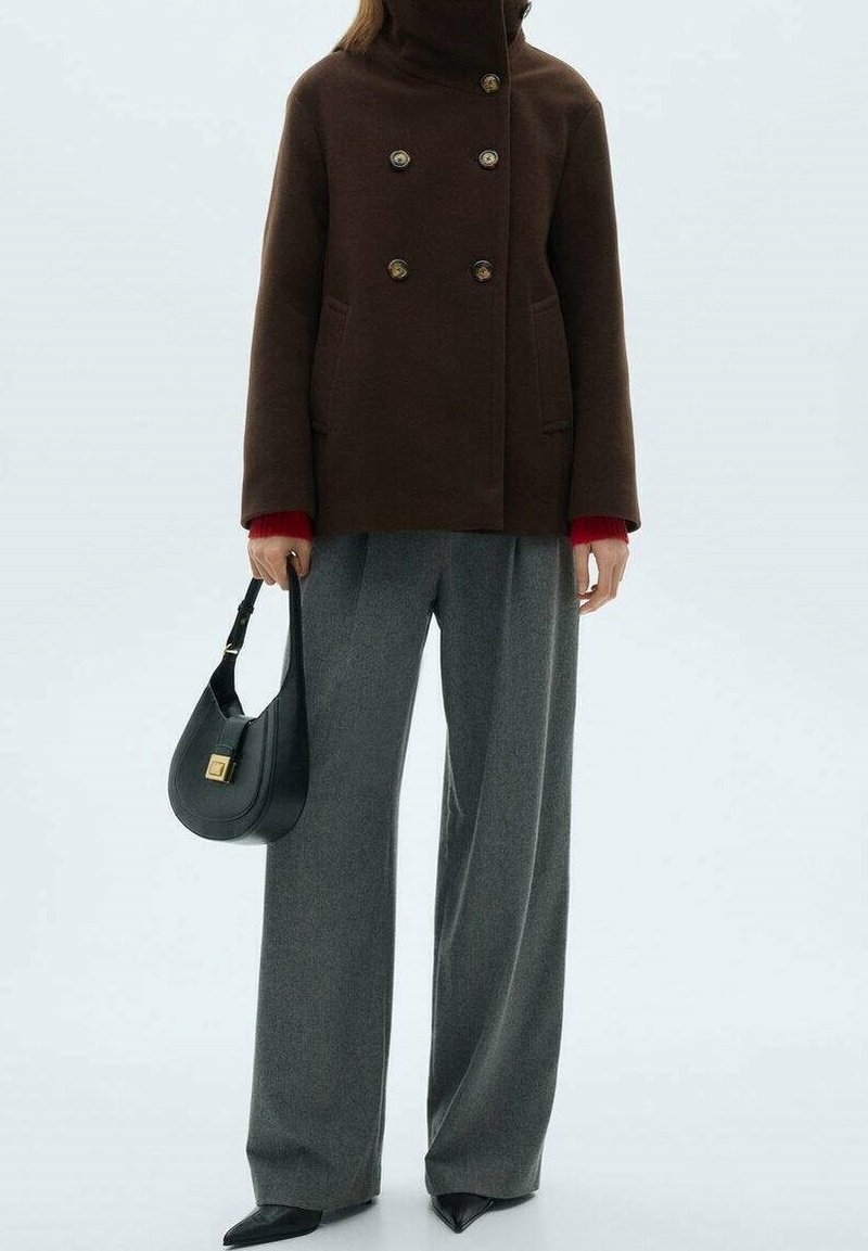 Abrigo marrón de doble botonadura con botones metálicos, cuello alto, combinado con pantalones grises de pierna ancha y un bolso negro con detalles dorados.