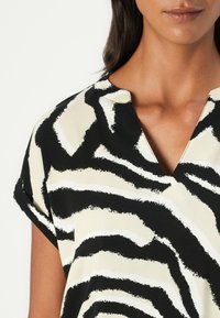 Blouse à manches courtes avec un imprimé zèbre noir et blanc, décolleté en V et en tissu doux et fluide pour un ajustement décontracté.
