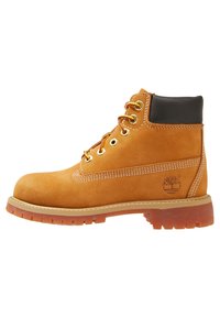 Stivale in suede marrone chiaro con colletto nero, occhielli in metallo giallo, lacci rossi e suola in gomma marrone con un motivo di grip testurizzato.