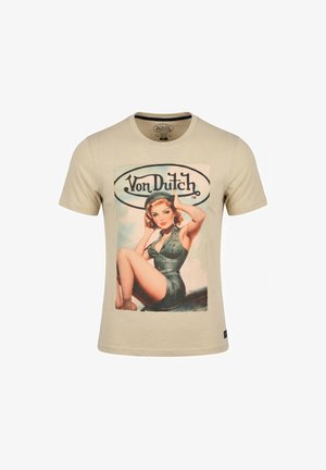 T-shirt beige Von Dutch avec une pin-up vintage en tenue verte assise sur l'aile d'un avion et le logo Von Dutch au-dessus d'elle.