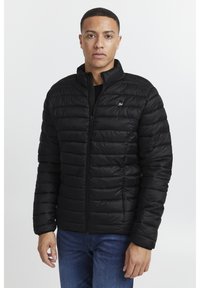 Black puffer jacket with a zip front, high collar, and quilted texture. Features a small logo on the chest and banded cuffs.