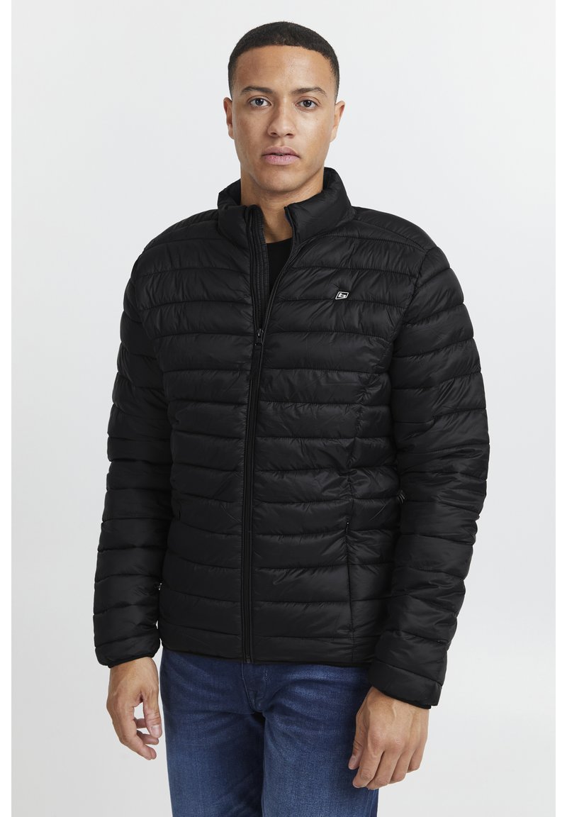 Black puffer jacket with a zip front, high collar, and quilted texture. Features a small logo on the chest and banded cuffs.