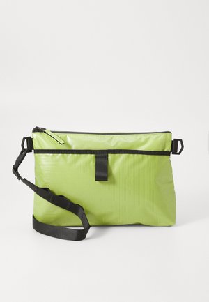 Borsa in tessuto verde, testurizzata, con chiusura a zip, dettagli neri e tracolla regolabile, caratterizzata da un design minimalista e rettangolare.