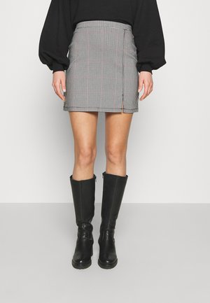 Zwart-witte houndstooth mini-rok met een zijsplit, gecombineerd met zwarte leren laarzen tot de knie. Glad textuur, aansluitend ontwerp.