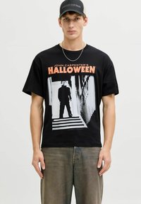 Crna pamučna majica s grafičkim otiskom figure iz "Halloween" s narančastim tekstom. Uparena s izblijedjelim sivim trapericama.