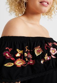Czarna bluzka sestra z odkrytymi ramionami z kolorową koronką w kwiaty, teksturowana elastyczna dekolt oraz koronkowe wykończenie na dole.