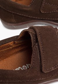 Scarpe slip-on in suede marrone con una consistenza morbida, caratterizzate da un risvolto prominente e cuciture in contrasto lungo i bordi.