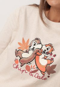 Sudadera de color beige claro con los personajes Chip y Dale, rodeados de coloridas hojas de otoño y bellotas, con el texto "Chip & Dale" debajo.