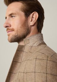 Blazer marrone a quadri con colletto alto, realizzato in tessuto texture. Caratterizzato da una finitura pulita e dettagli di cucitura discreti.