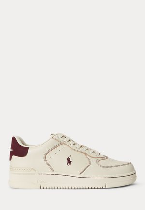 Niedriger cremefarbener Sneaker mit bordeauxrotem Fersenpatch und Logo, Schnürung vorne und strukturierter Sohle, entworfen für den Freizeitgebrauch.