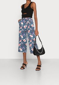 Top corto nero, pantaloni a palazzo blu con stampa floreale, borsa nera con dettagli in catena e sandali neri con tacco e apertura davanti.