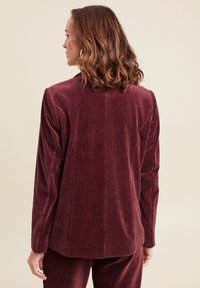 Burgunderfarbener Cord-Blazer mit vertikalen Rippungen, ausgestattet mit einem einzelnen Rückenschlitz und angedeuteten Revers, entworfen für eine taillierte Passform.