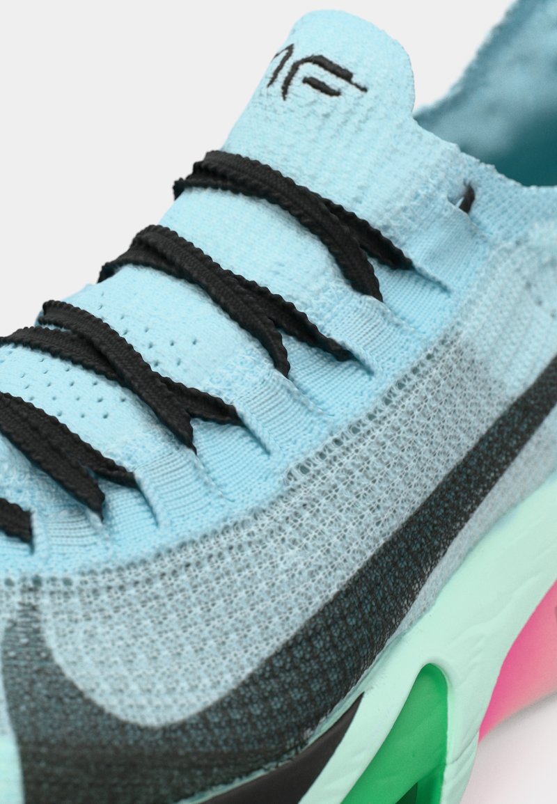 Zapatilla deportiva de color azul claro con cordones negros, parte superior de malla, acentos grises y una suela multicolor con detalles en verde, rosa y negro.