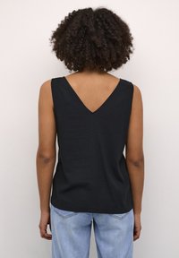 Sort sansærmet top med V-hals design, lavet af letvægtsstof. Enkel, afslappet pasform med lige søm, båret med lyseblå jeans.