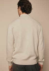 Lys beige sweater med lange ærmer, ribbede manchetter og kant. Blød tekstur, enkelt design og en tætsiddende silhuet. Enkelt uden mønstre eller accenter.
