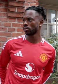 Raudona Manchester United futbolo marškinėliai su baltais akcentais. Savybėje komandos logotipas, rėmėjo logotipas ir trys juostelės ant pečių.